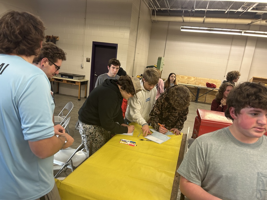 Students signing holiday cards at a table in a school workshop