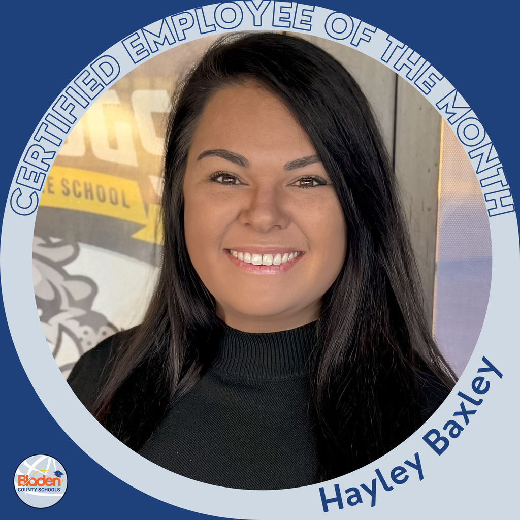 A woman with long dark hair smiles brightly while wearing a black turtleneck. A school-themed banner is visible in the background. The photo is encircled by a blue-and-gray “Certified Employee of the Month” frame with the name “Hayley Baxley” at the bottom.