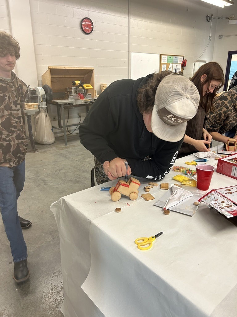 a student carefully adds red icing to a gingerbread tractor