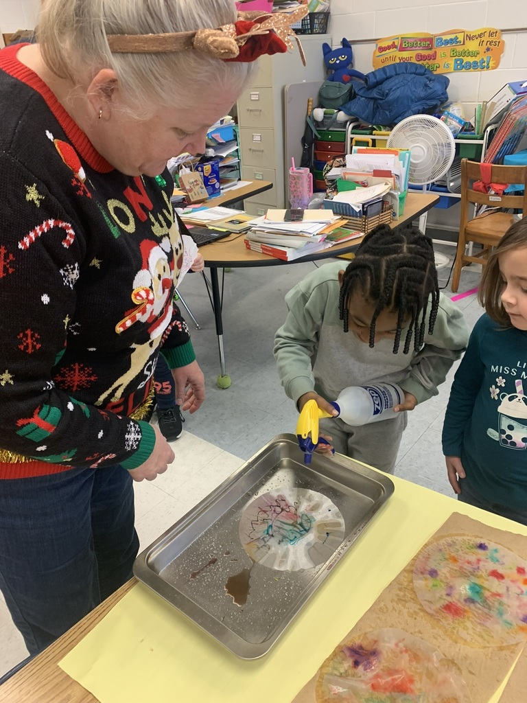 A teacher assists a student as they spray water onto a coffee-filter snowflake, watching the colors blend and flow across the paper.