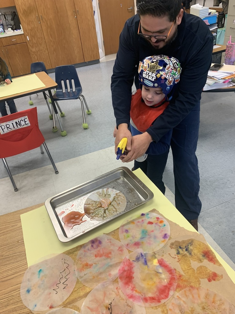 A teacher assists a student as they spray water onto a coffee-filter snowflake, watching the colors blend and flow across the paper.