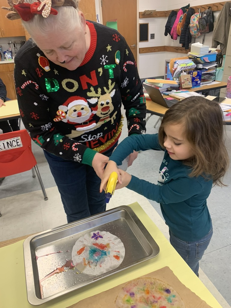 A teacher assists a student as they spray water onto a coffee-filter snowflake, watching the colors blend and flow across the paper.