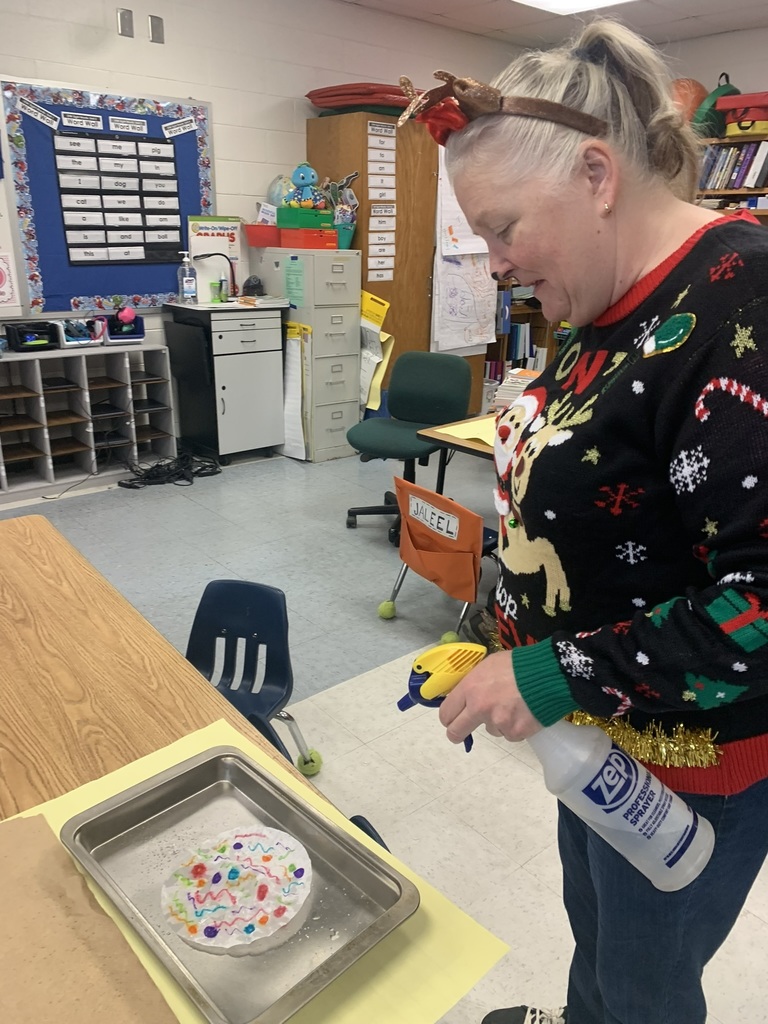 A teacher assists a student as they spray water onto a coffee-filter snowflake, watching the colors blend and flow across the paper.