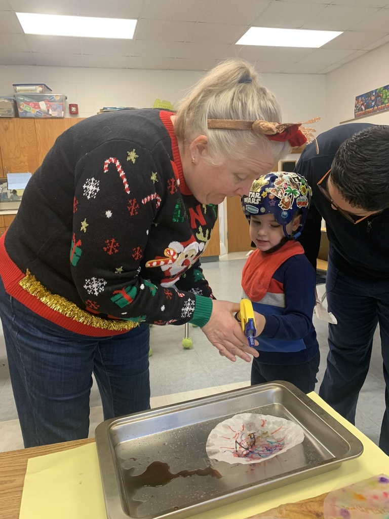 A teacher assists a student as they spray water onto a coffee-filter snowflake, watching the colors blend and flow across the paper.
