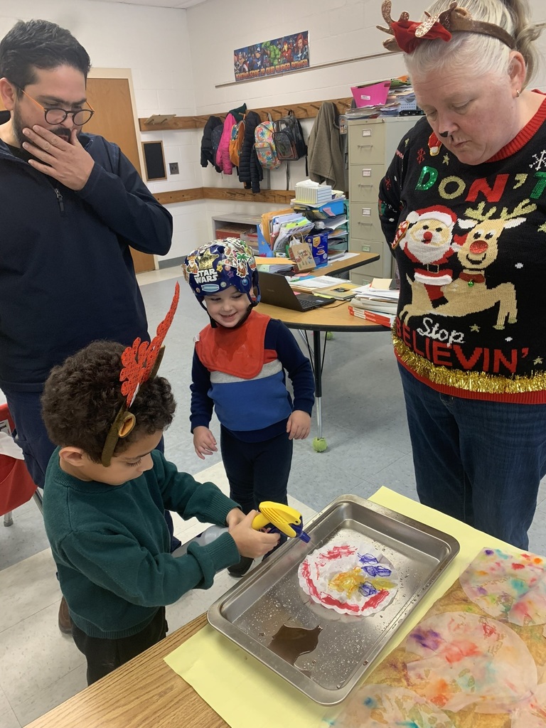 A teacher assists a student as they spray water onto a coffee-filter snowflake, watching the colors blend and flow across the paper.