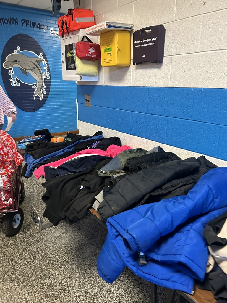 ables in the front lobby of Elizabethtown Primary School filled with lost and found items including coats, jackets, hoodies, and sweaters in various colors.