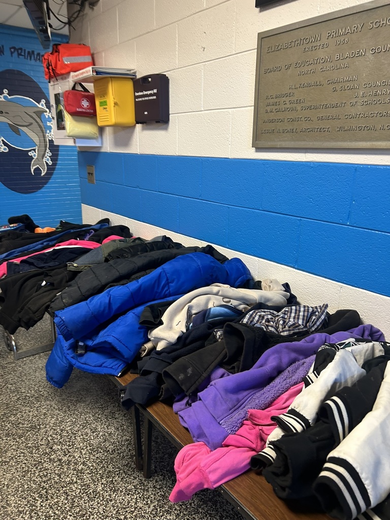 ables in the front lobby of Elizabethtown Primary School filled with lost and found items including coats, jackets, hoodies, and sweaters in various colors.