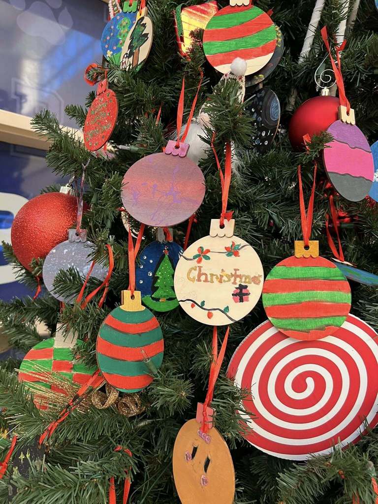 Another close-up of the Christmas tree featuring handmade student ornaments, candy-cane designs, striped baubles, and a “Christmas” painted ornament.