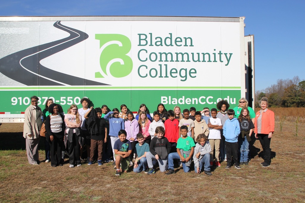 A large group of students and adults pose for a photo outdoors in front of a Bladen Community College mobile unit during a field trip.