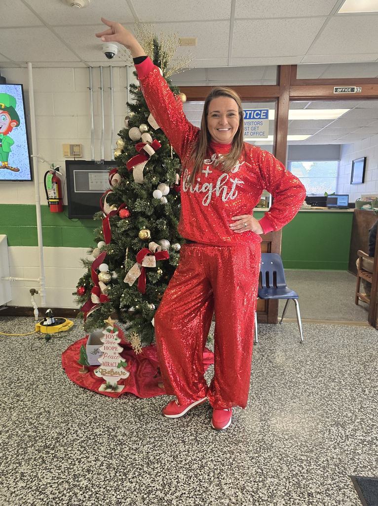 A staff member poses confidently in front of a decorated Christmas tree, wearing a bright red, sequined holiday outfit.