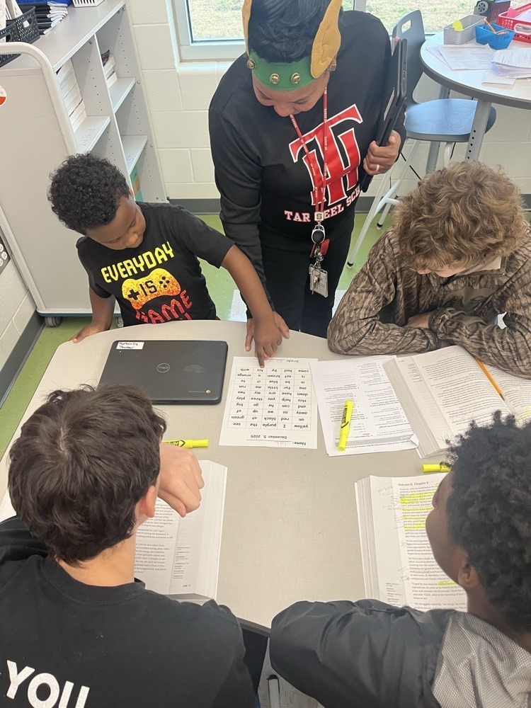 A teacher supports a group of students at a table, guiding them through a reading assignment during small-group instruction.