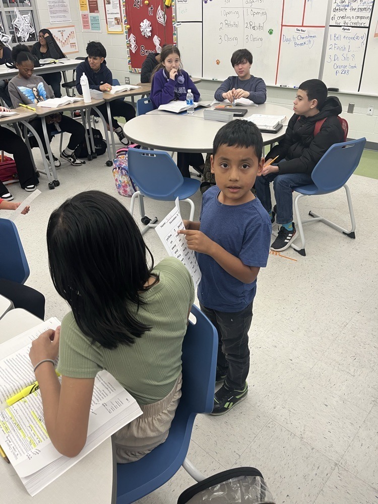 Elementary students work together in small groups, reading and discussing a worksheet during a classroom activity.