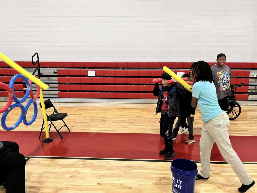 Students throw foam noodles at a target as part of a fun, inclusive field day game in the gymnasium.