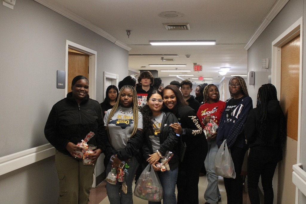 A large group of students and adults pose together in front of a decorated Christmas tree, celebrating a successful holiday service project.