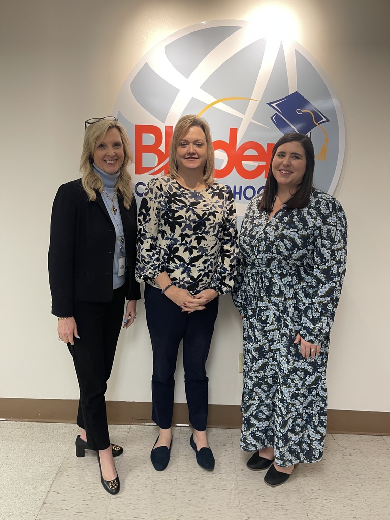 Three Bladen County Schools staff members stand in front of the district logo wall, smiling for a photo inside the central office.