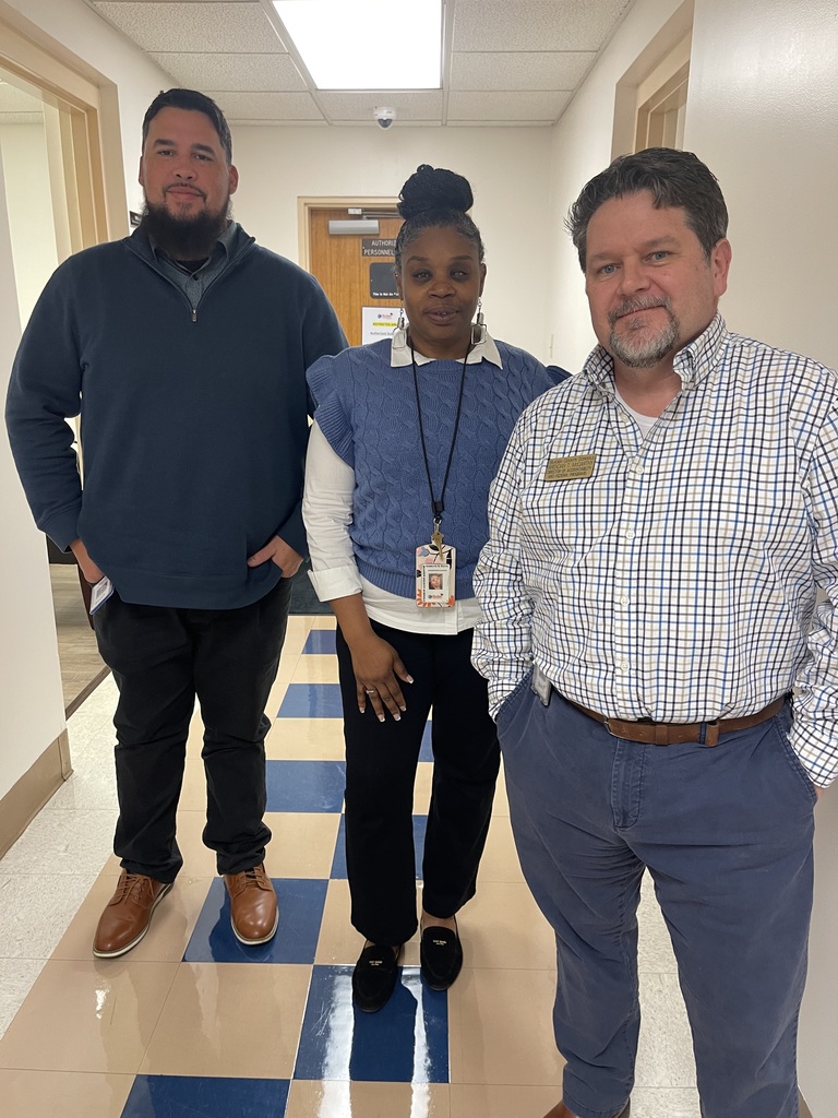 Three Bladen County Schools staff members stand together in a hallway, posing for a photo inside a school or district office building.