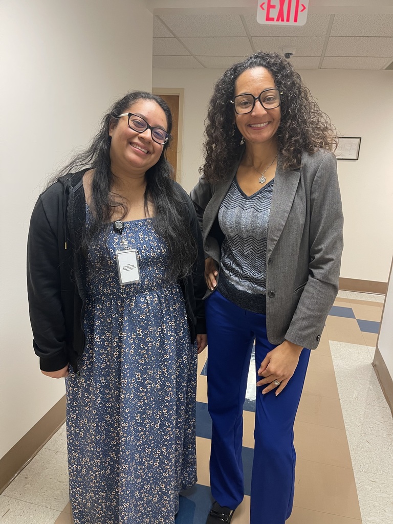 Two Bladen County Schools staff members smile while standing in a hallway, wearing professional attire and staff identification badges.