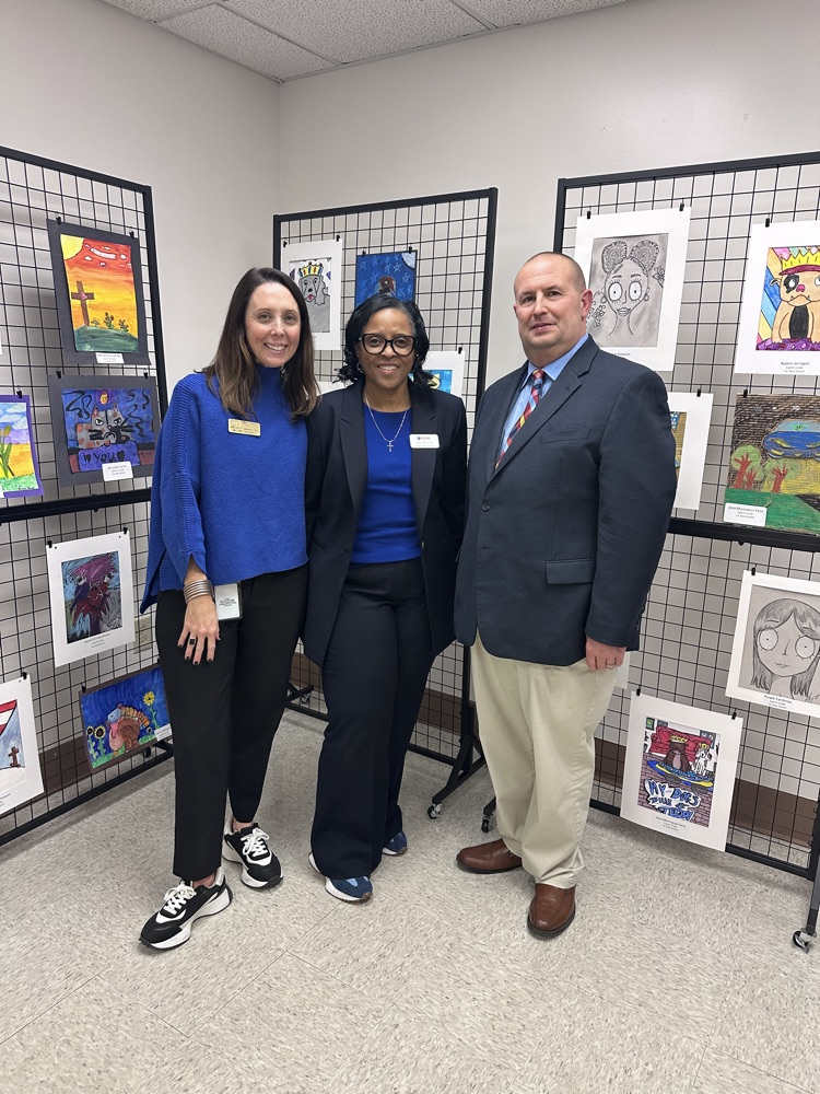 three district office members stand together wearing blue in front of student artwork.