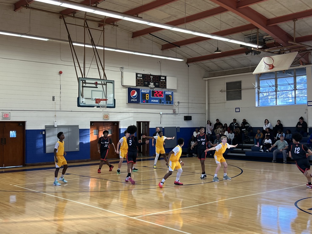 Boys basketball players set up on offense near the three-point line as the scoreboard shows time remaining in the period.