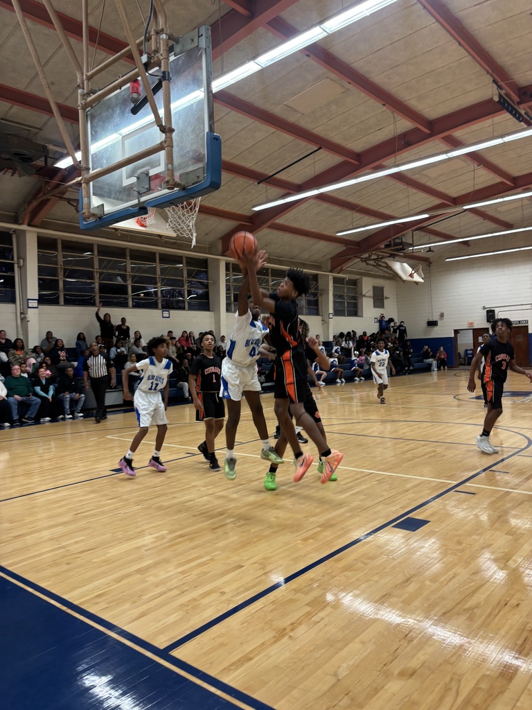 Boys basketball players jump near the basket as one attempts a contested shot while teammates and opponents position for a rebound.