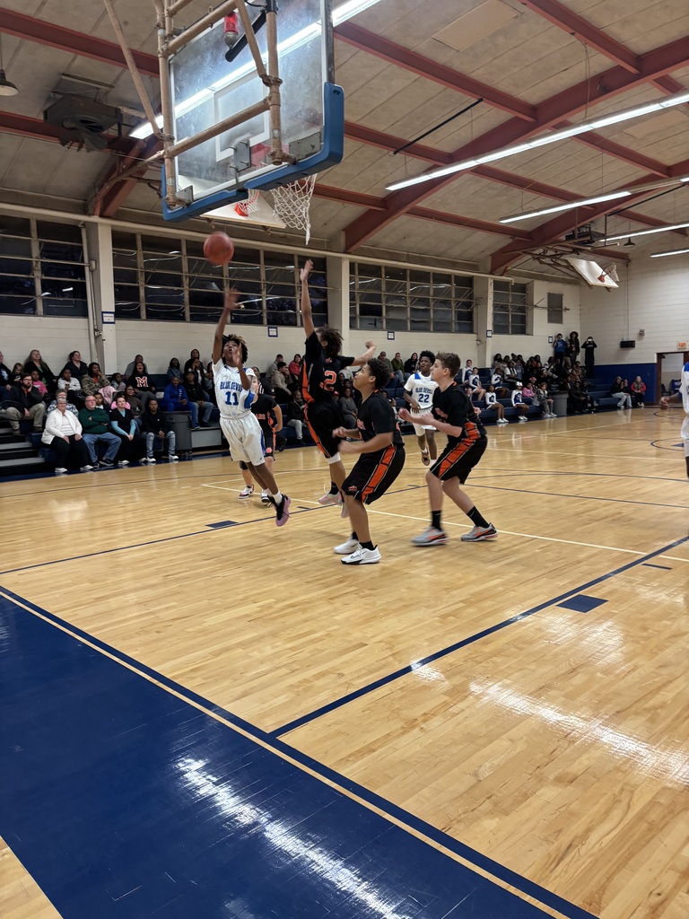 A boys basketball player drives toward the hoop for a layup as defenders jump to contest the shot in a crowded lane.