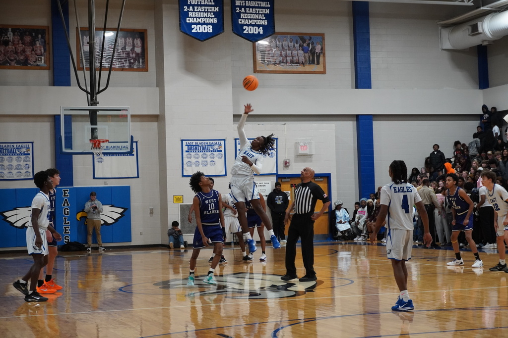 A boys basketball player leaps for a layup as defenders reach to contest the shot beneath the basket.