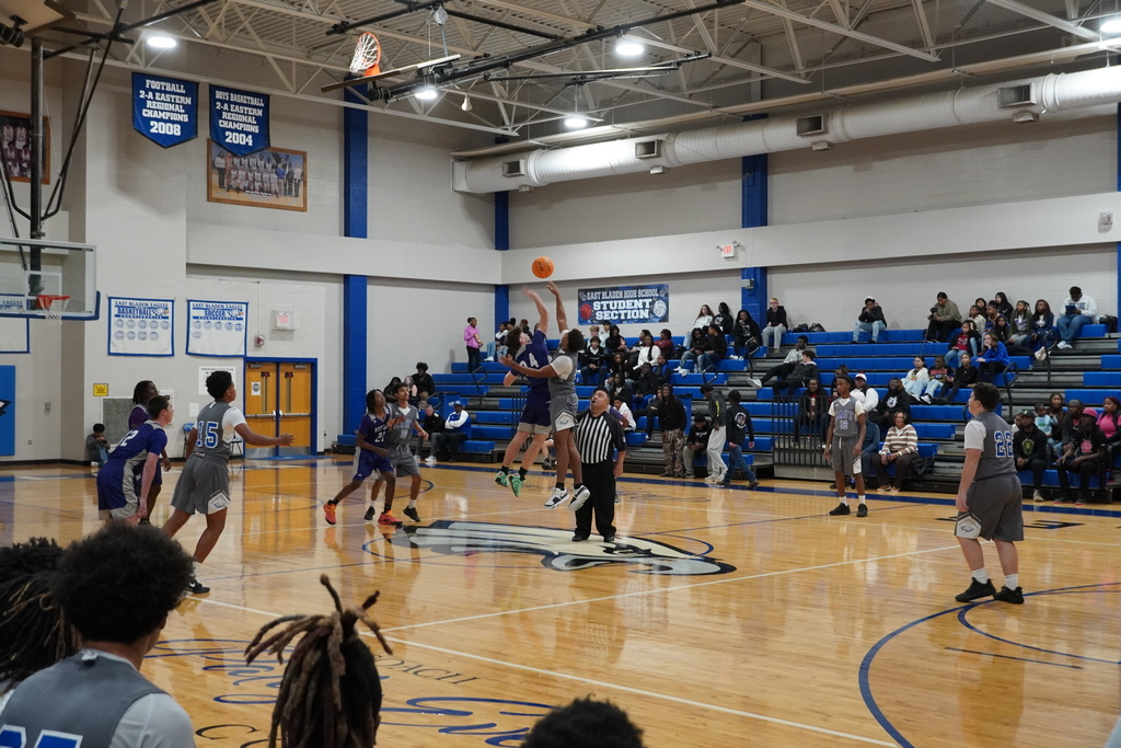 Boys basketball players leap for the opening tip at center court as the referee tosses the ball to start the game.