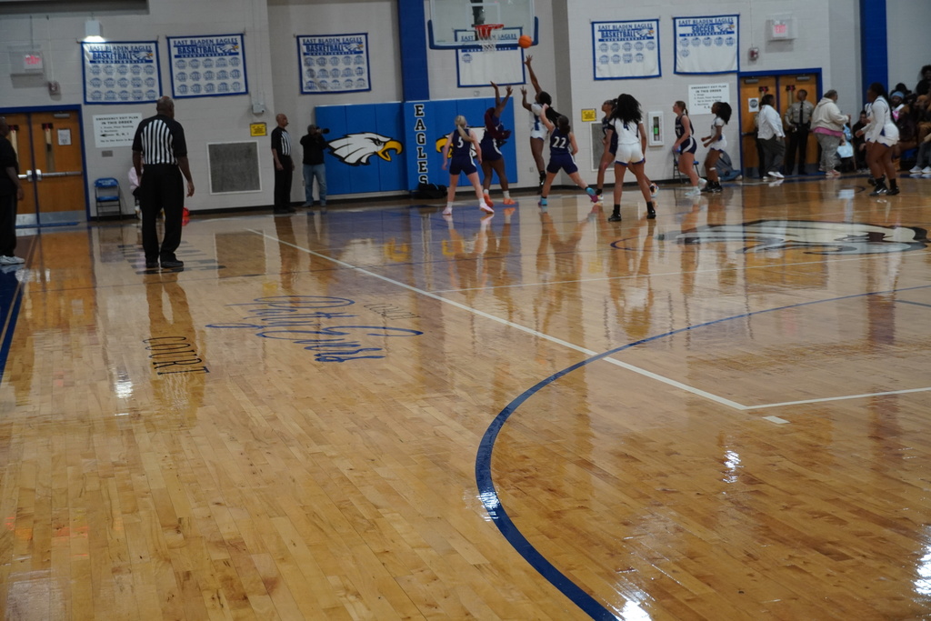Girls basketball players converge in the paint as one attempts a shot near the basket during a fast-paced sequence.