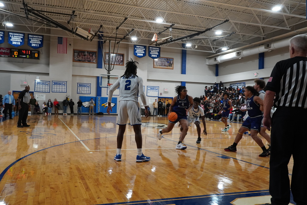 A boys basketball player dribbles toward the lane while teammates and defenders spread across the court during live action.