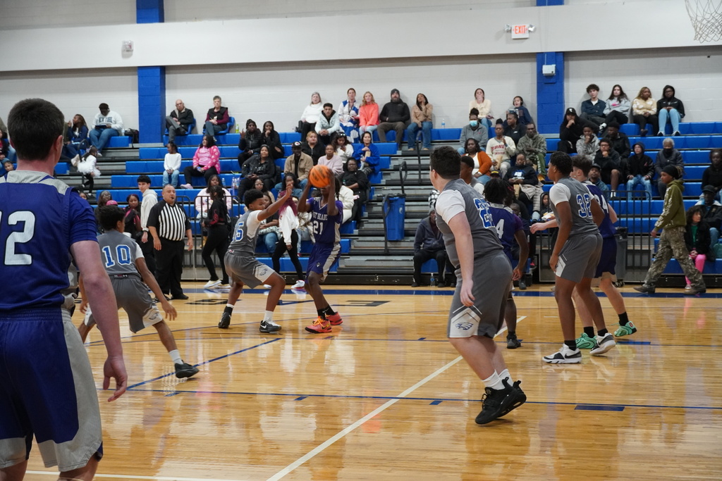 A boys basketball player in a dark uniform catches the ball near the lane while defenders close in and teammates move into position.