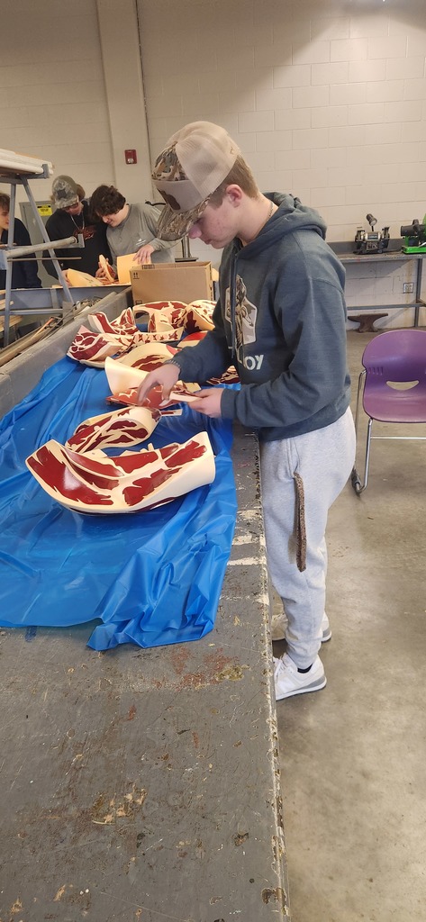 A student wearing a hat organizes painted 3D models of meat cuts on a table covered in a blue protective tarp.