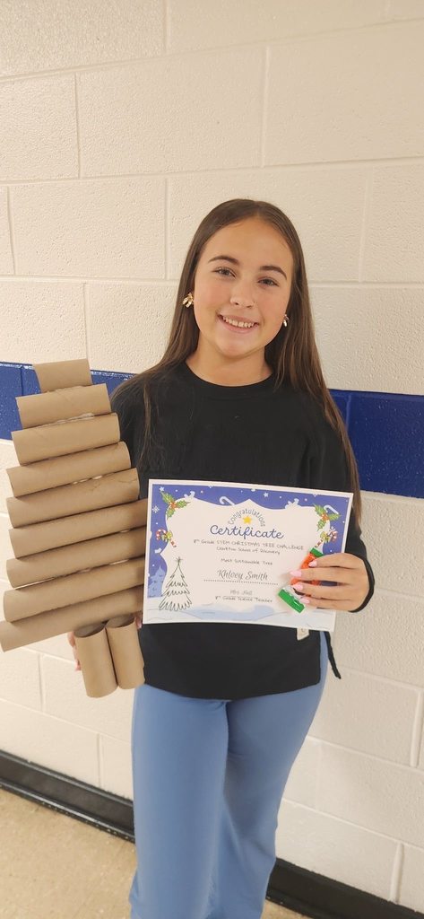A student holds a certificate and a Christmas tree made from stacked cardboard tubes for the STEM Christmas Tree Challenge.