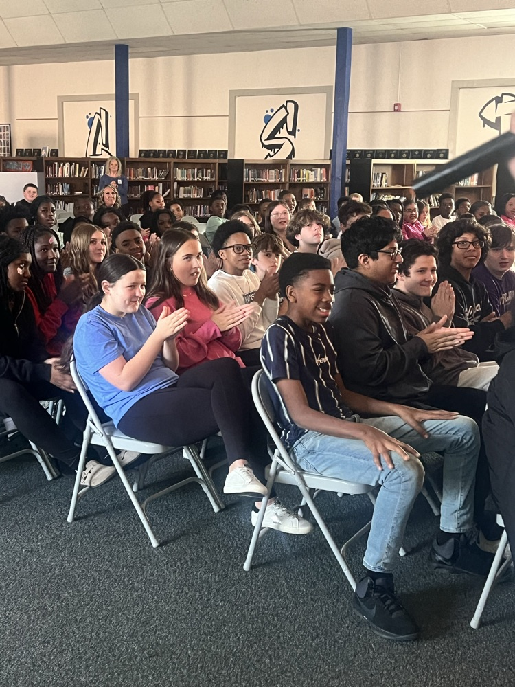 Students sitting in chairs watching people perform poetry