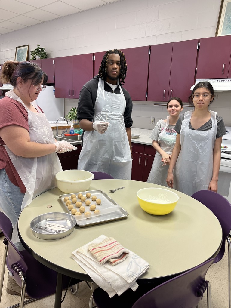 Four students working at a table, carefully arranging food items onto baking sheets in a school culinary arts classroom.