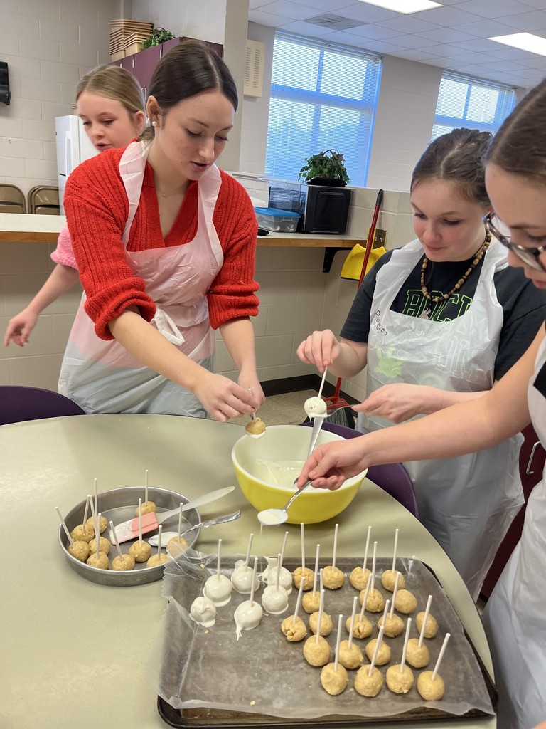 Close-up of three students collaborating to mix ingredients in a large metal bowl on a countertop.