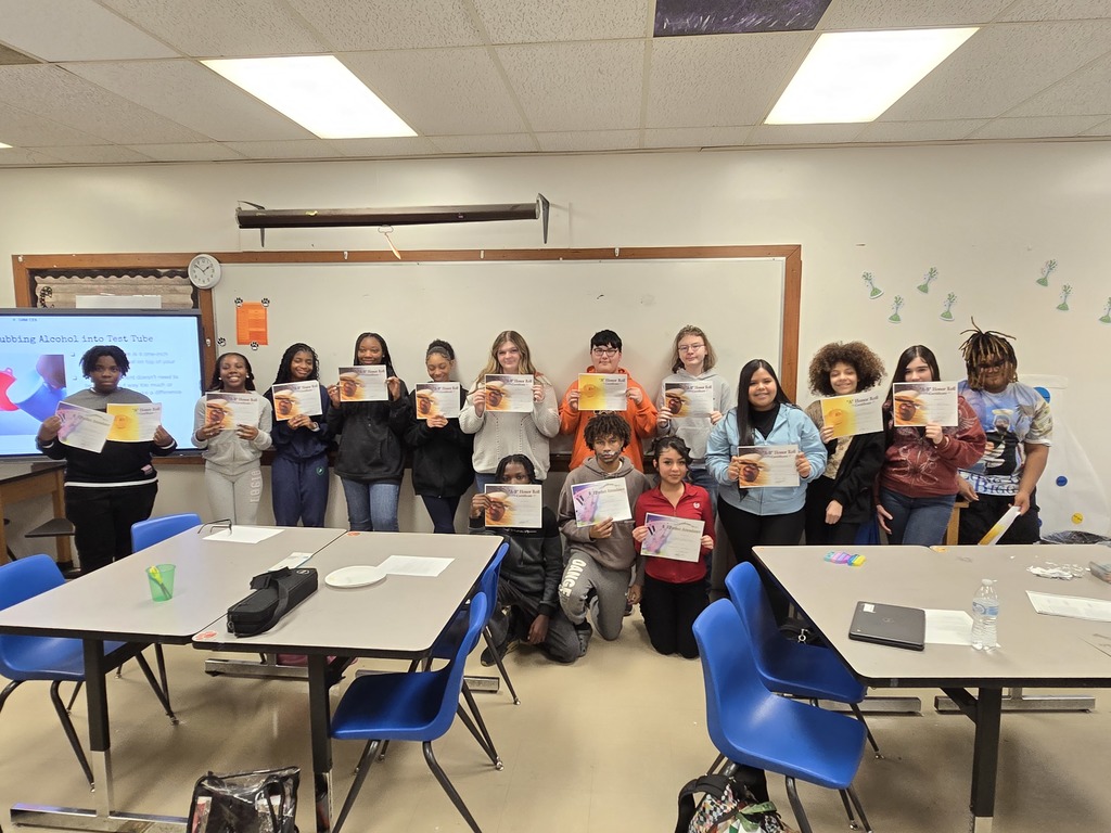 A large group of Elizabethtown Middle School students pose in a classroom holding Honor Roll and Perfect Attendance certificates during a student recognition celebration.