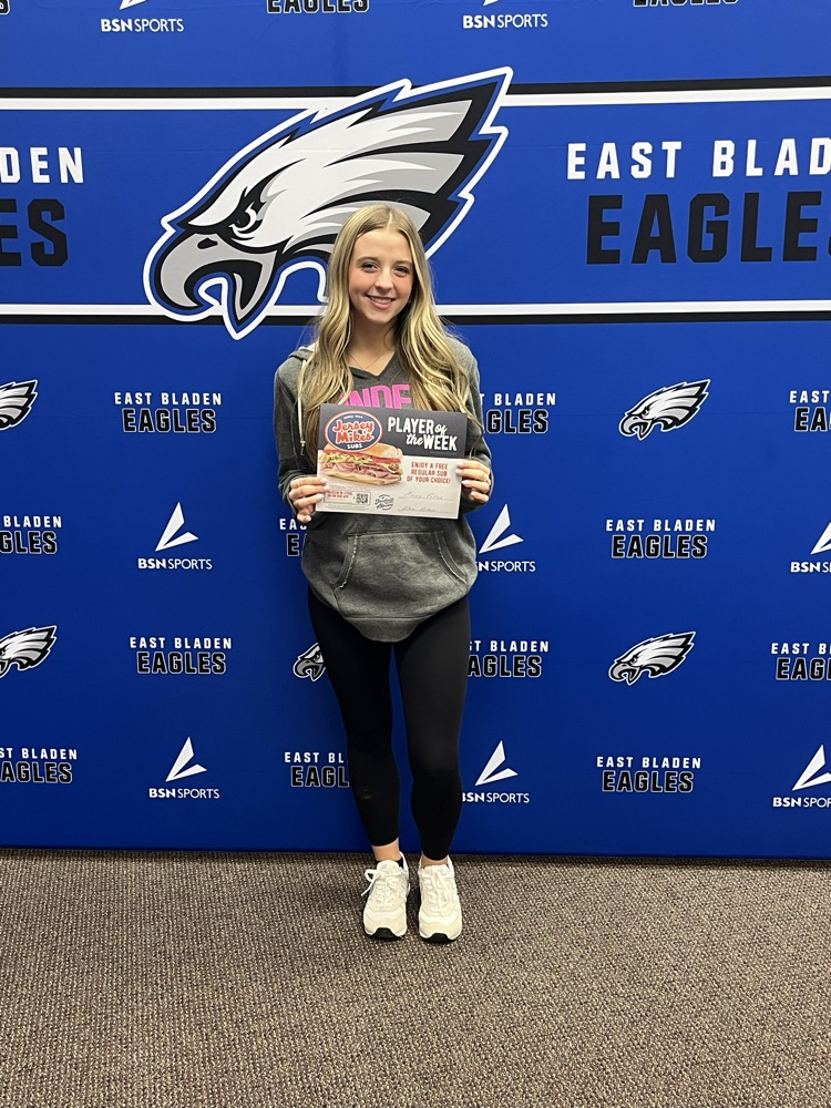 Macey Potter stands smiling in front of an East Bladen Eagles backdrop, holding a “Player of the Week” certificate.