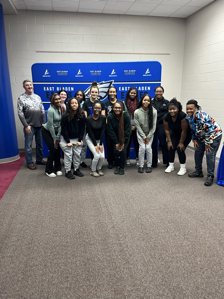 EB varsity girls basketball team With a gentleman and Coach in front of a blue East Bladen backdrop