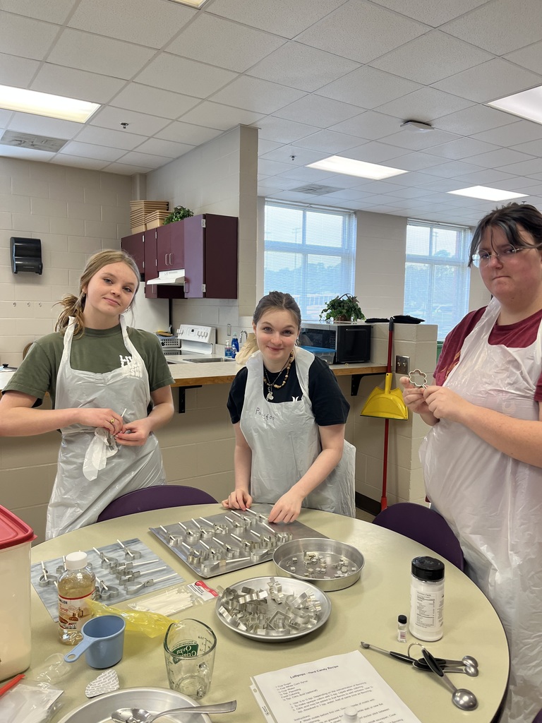 Three students in aprons and hairnets posing in a classroom kitchen during a food science lab.
