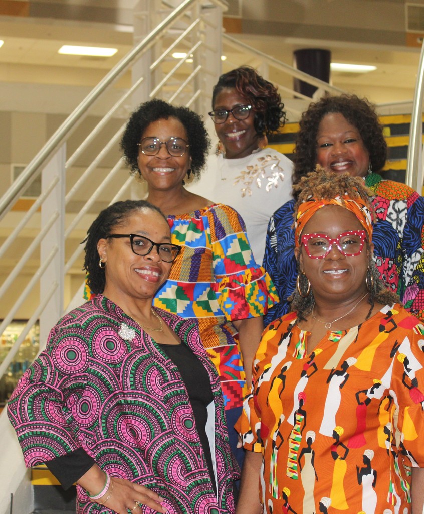 Six smiling Black women in vibrant, professional attire stand together on a staircase for a Black History Month celebration.