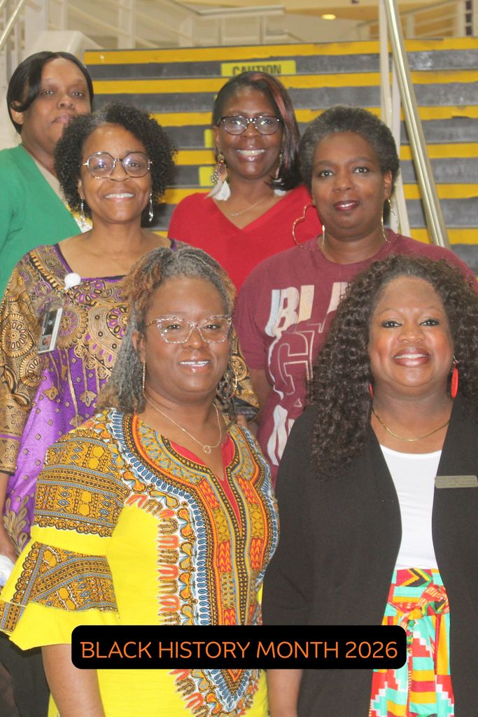 A group of six smiling Black women standing together on a staircase. They are dressed in colorful, professional attire, including shades of red, green, and purple.