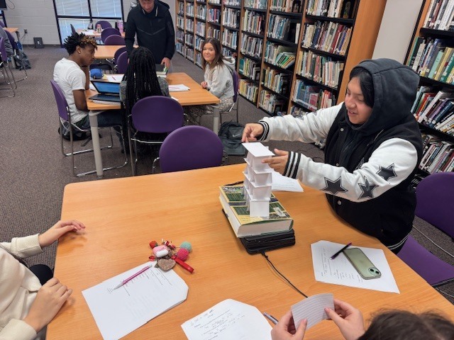 Students at West Bladen High School work together at a classroom table to build a tall tower out of white index cards and paper during a hands-on STEM activity.