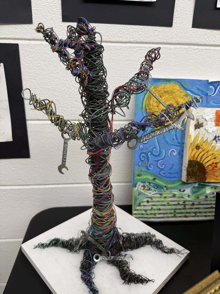 Abstract human figure sculpture made from wrapped and twisted multicolored wires, with small wrench details attached.