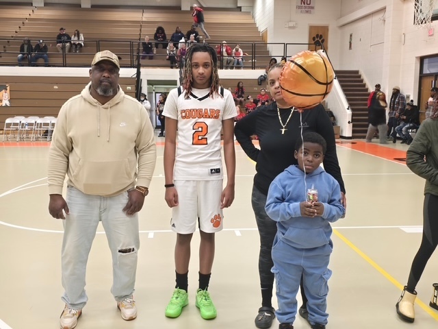 Cougars basketball player wearing jersey number 2 stands with family members on the court. A basketball balloon floats overhead as they pose for senior night.