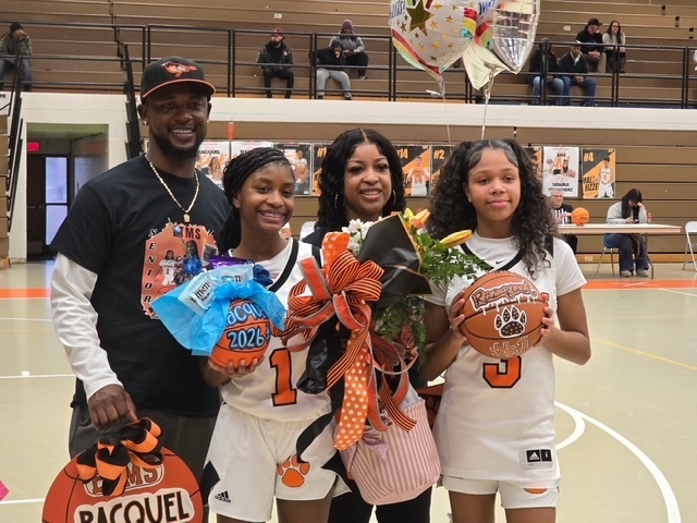 wo ETMS Lady Cougars basketball players stand with family members on the court holding flowers and basketball-themed gifts. Balloons and senior night posters are visible in the background.