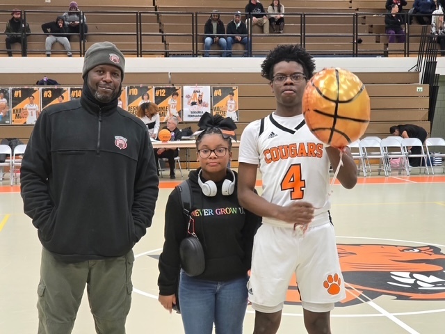 Cougars basketball player wearing jersey number 4 stands with family members on the court. A basketball-shaped balloon floats above them during senior night celebration.