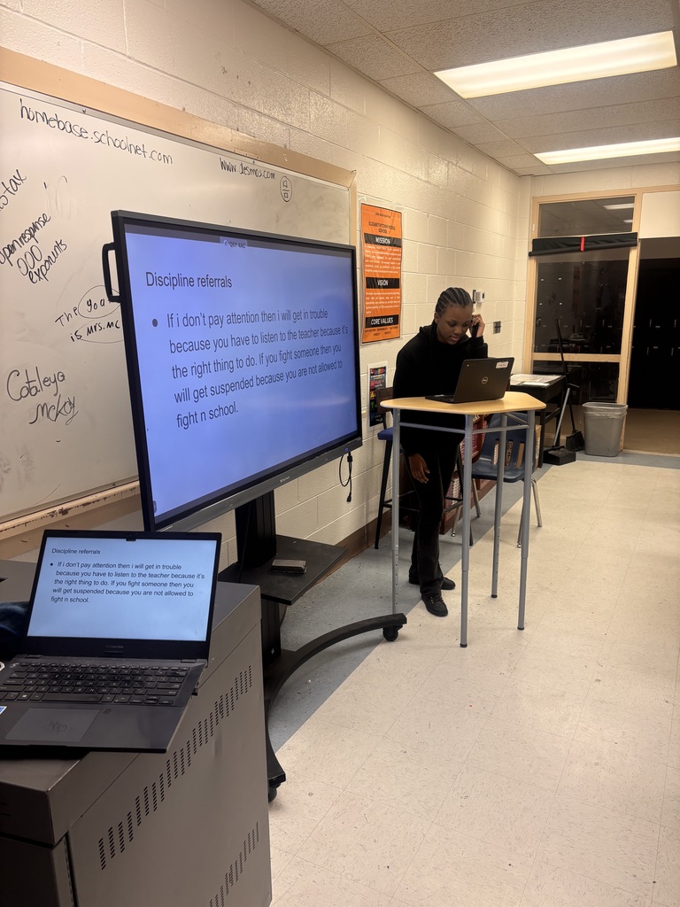 A student presents a slide about school discipline and responsibility while speaking to the class using a laptop and display screen.