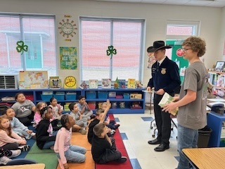 2 male FFA students speak to a class of elementary students sitting on a colorful carpet