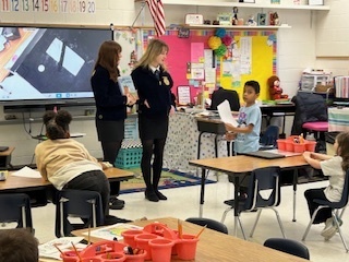 2 female FFA students talking to an elemntary boy holding a piece of paper while other elementary students observe