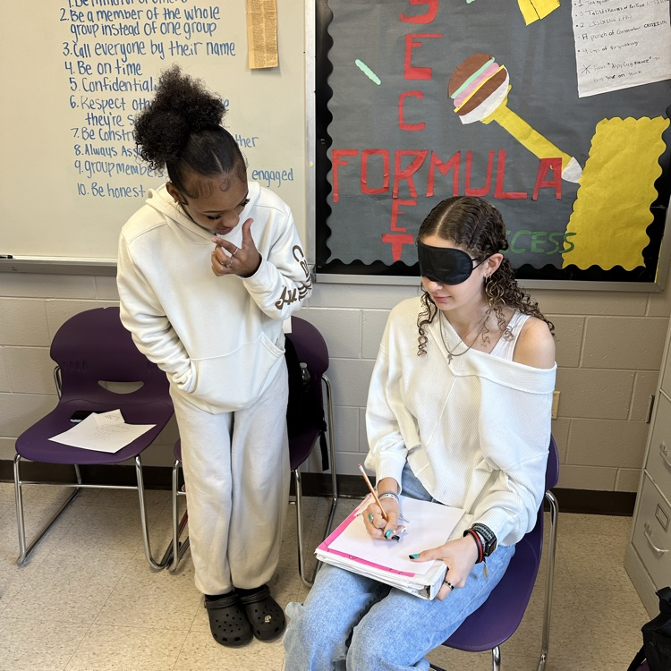 a student sits in a chair while another student stands next to the chair coaching her